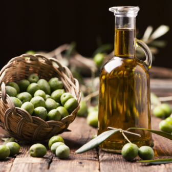 Wooden rustic table with Spanish olives displayed next to a glass of golden extra virgin olive oil